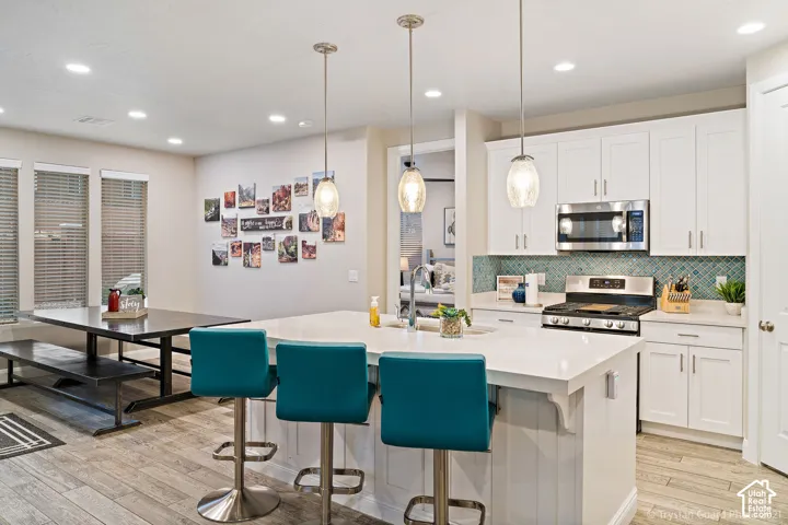Gourmet kitchen featuring white shaker cabinetry, stainless steel appliances, a large center island with pendant lighting, a patterned backsplash, and tile flooring