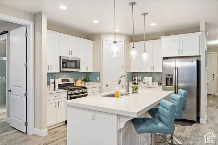 White cabinetry, stainless steel appliances, patterned tile backsplash, recessed lighting, and tile flooring