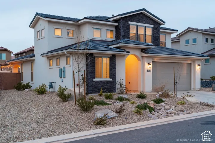Stucco exterior with stone veneer accents, multi-pane windows, arched entryway, two-car garage, and a low-maintenance landscape