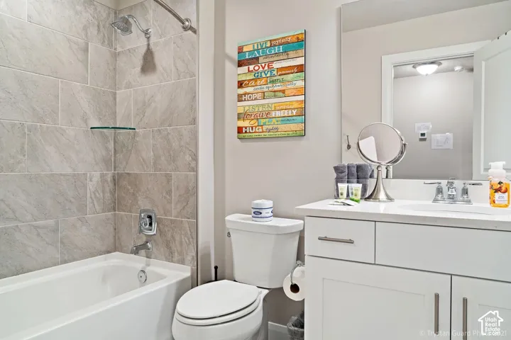Built-in bathtub with subway tile surround and glass shelf, a toilet, and a vanity with an integrated sink and mirror