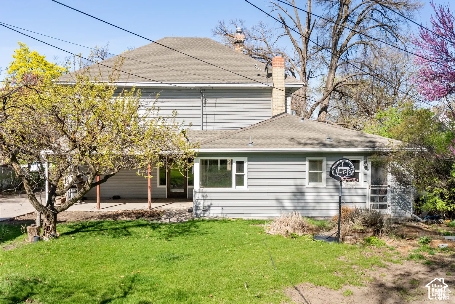 Multi-level home featuring light gray siding, a covered patio, and a shingled roof