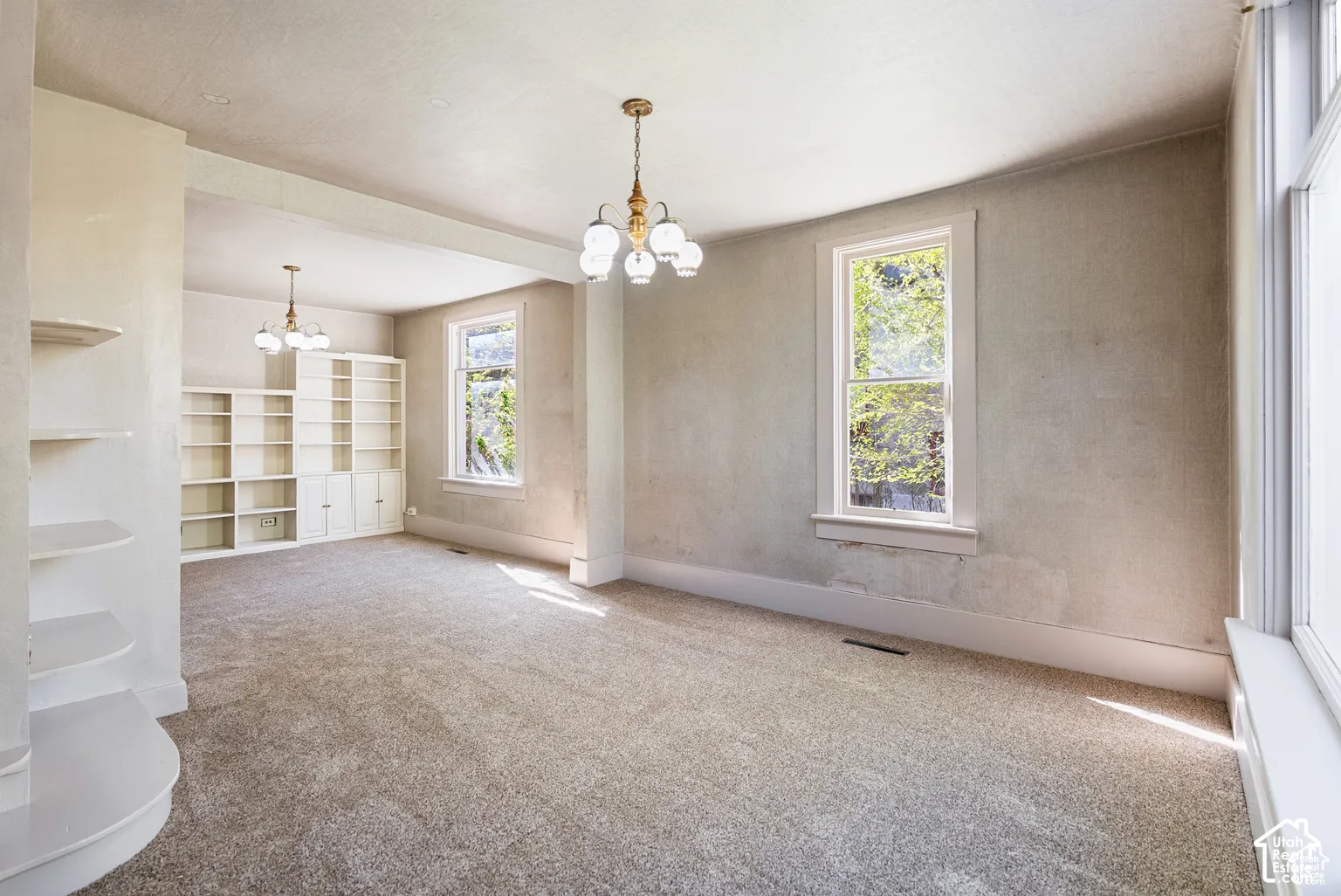 Carpeted room with multiple windows, built-in shelving, and two decorative chandeliers