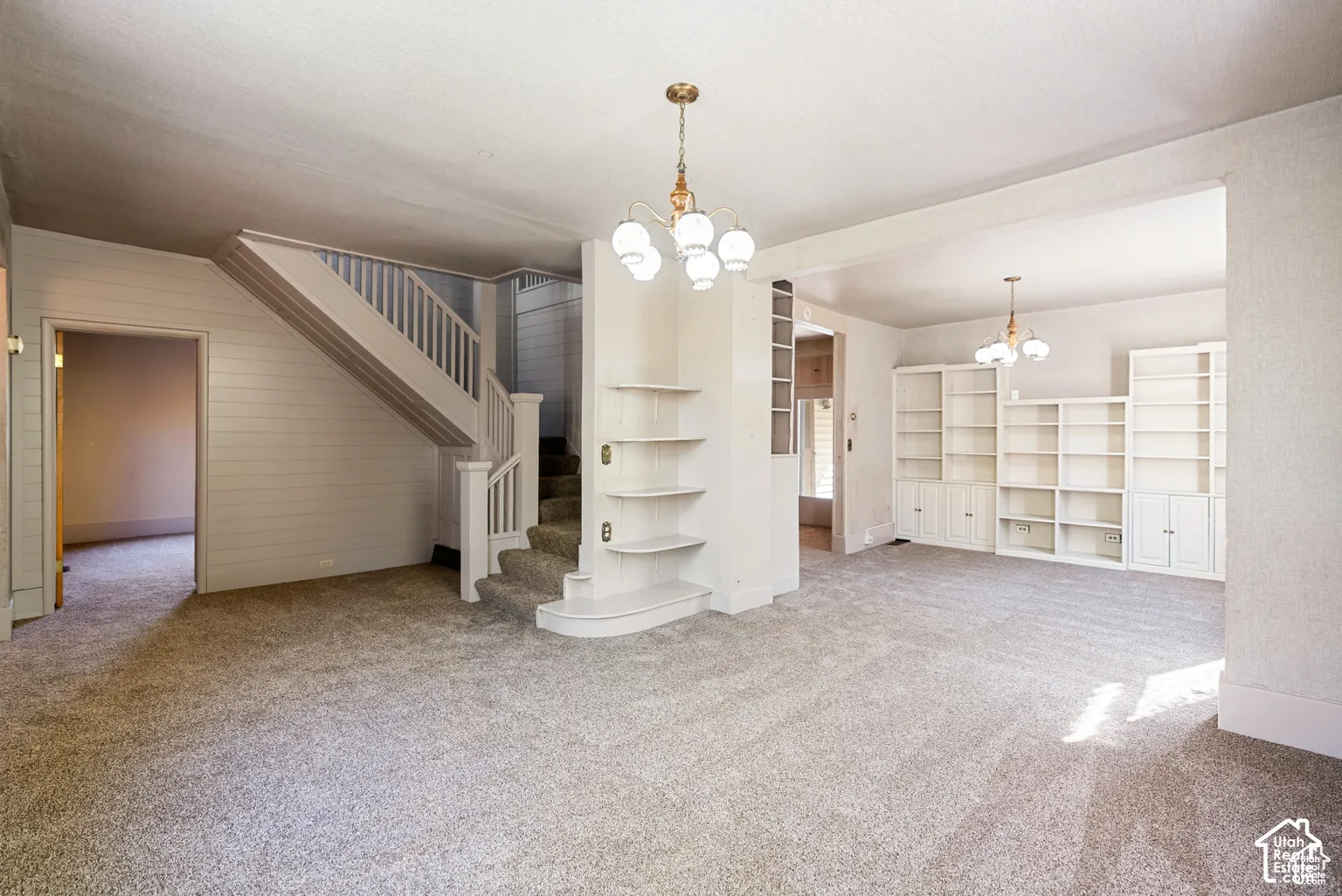 Carpeted living space featuring an open staircase with wood banister, built-in shelving, and two ceiling-mounted light fixtures
