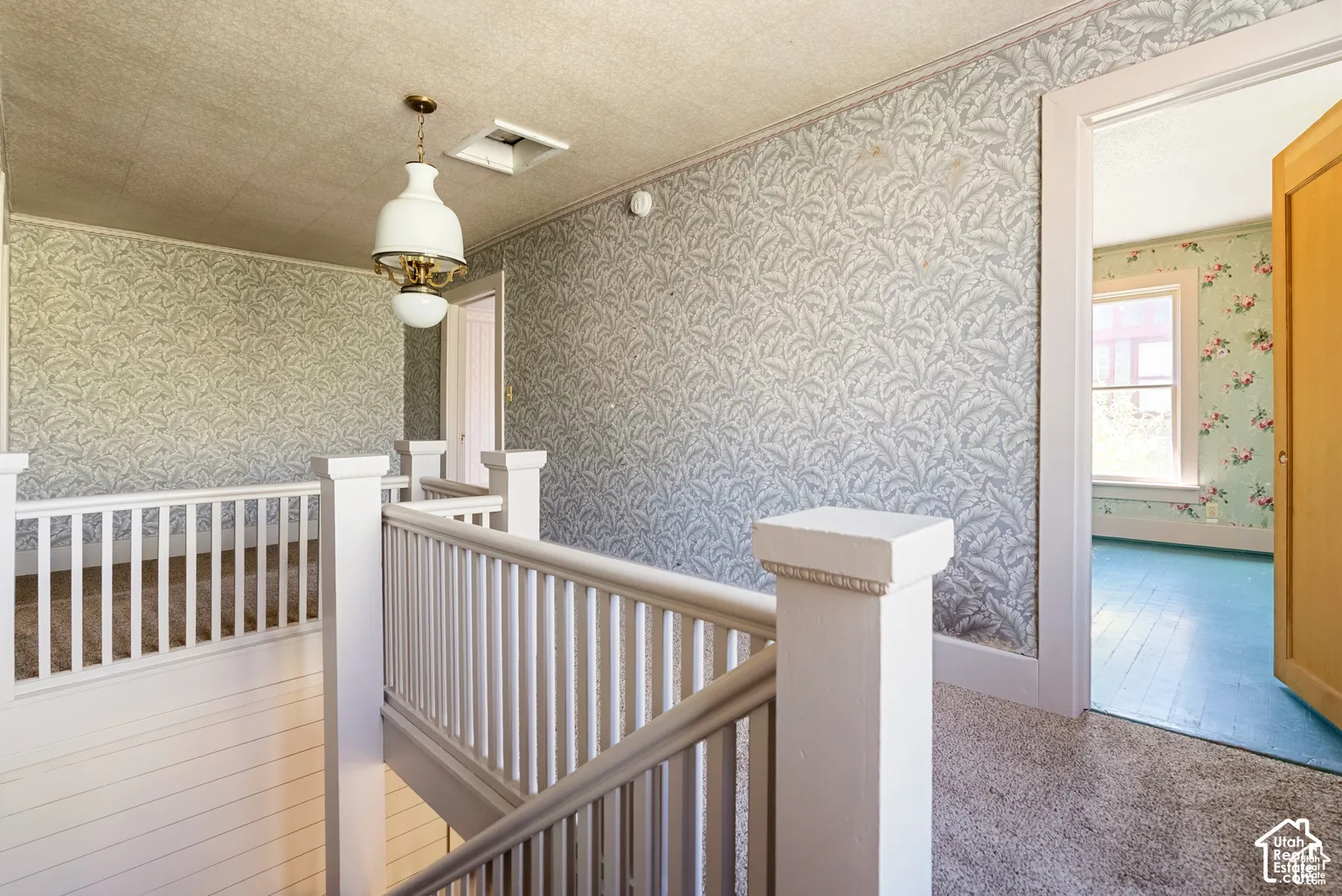 Upper-level landing with patterned wallpaper, white spindle railings, and a central pendant light fixture
