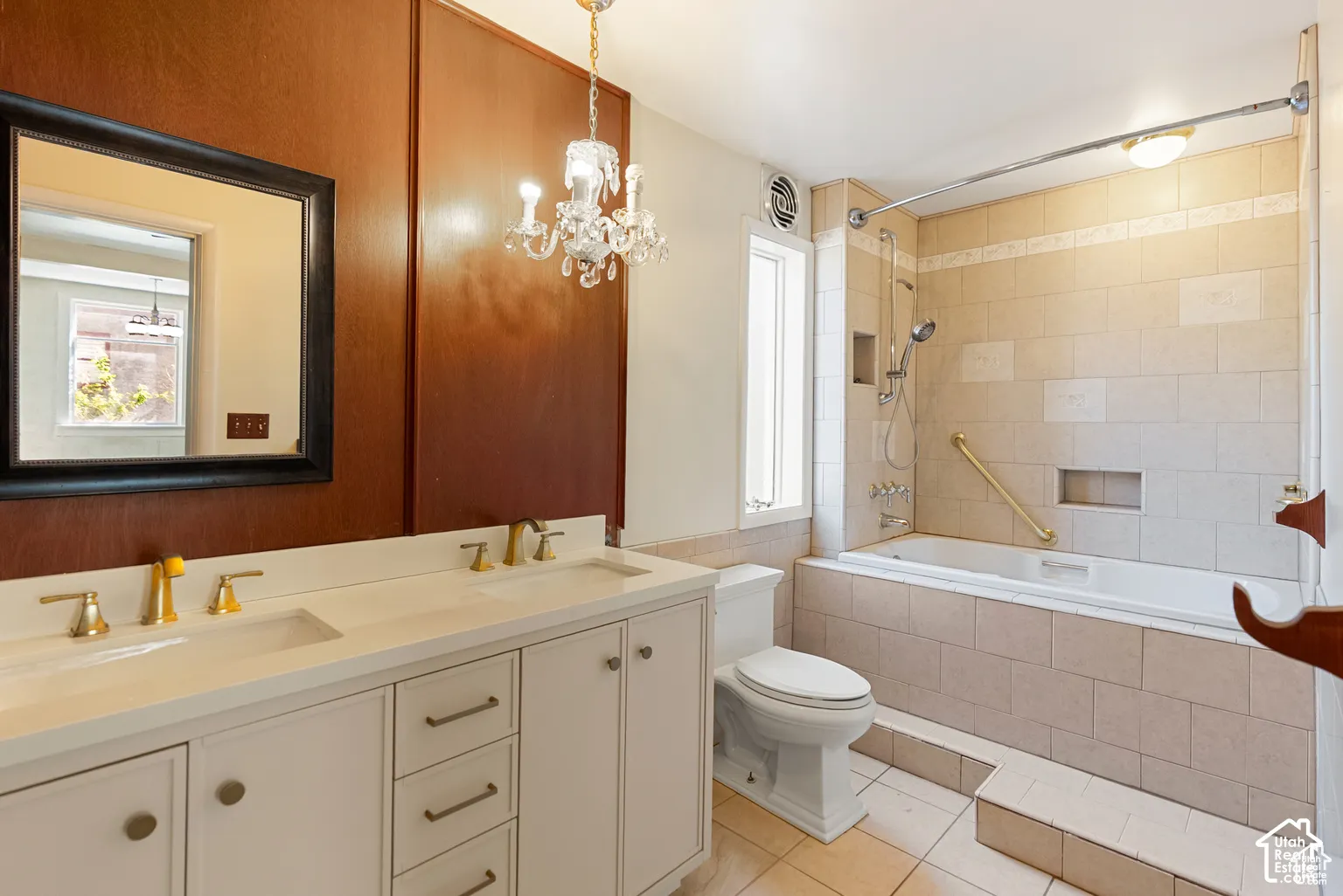 Double vanity with integrated sinks, gold-tone fixtures, wood paneling, tile-surround bathtub, and tiled flooring