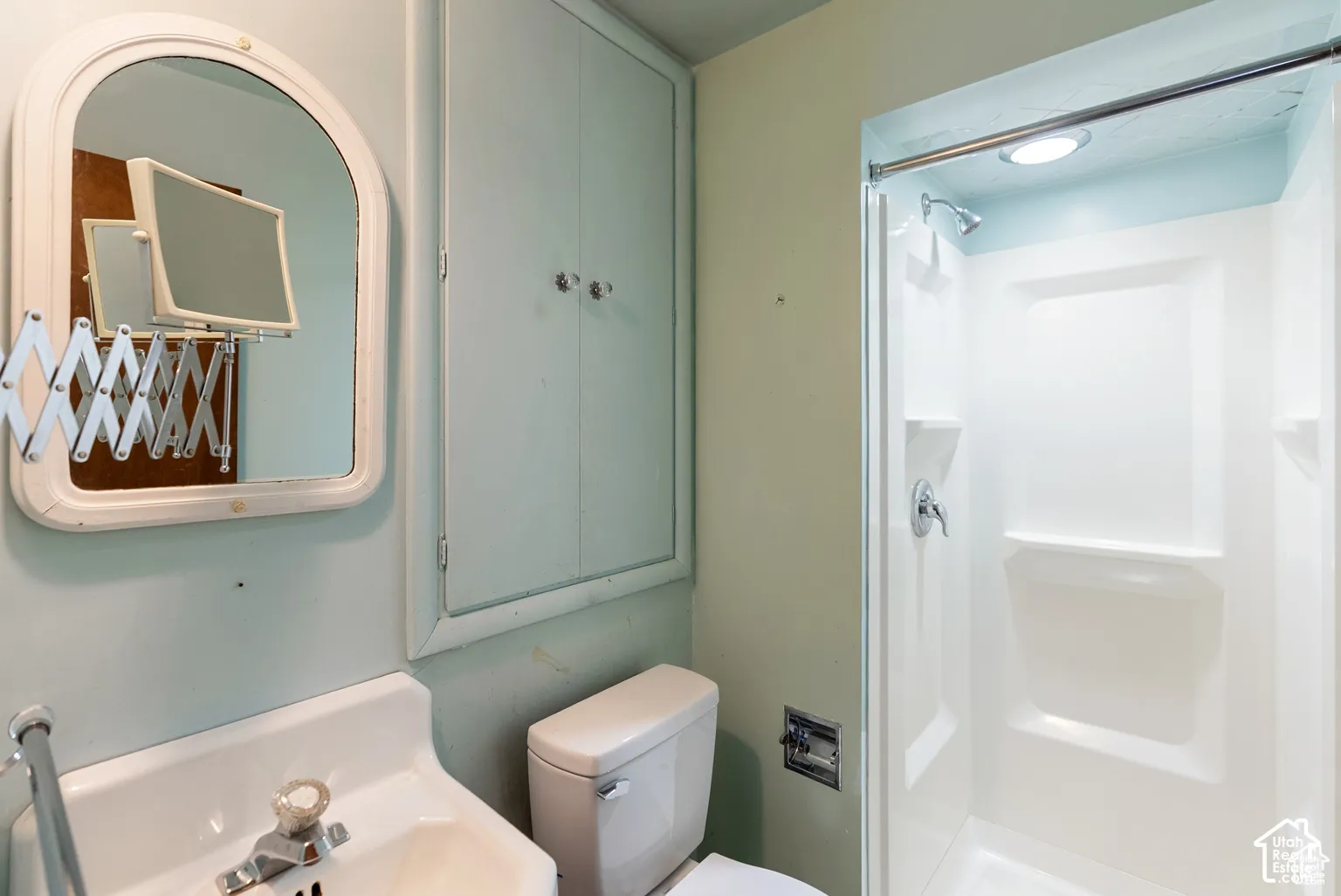 White pedestal sink, built-in storage cabinet, compact toilet, and a white shower stall with a chrome fixture