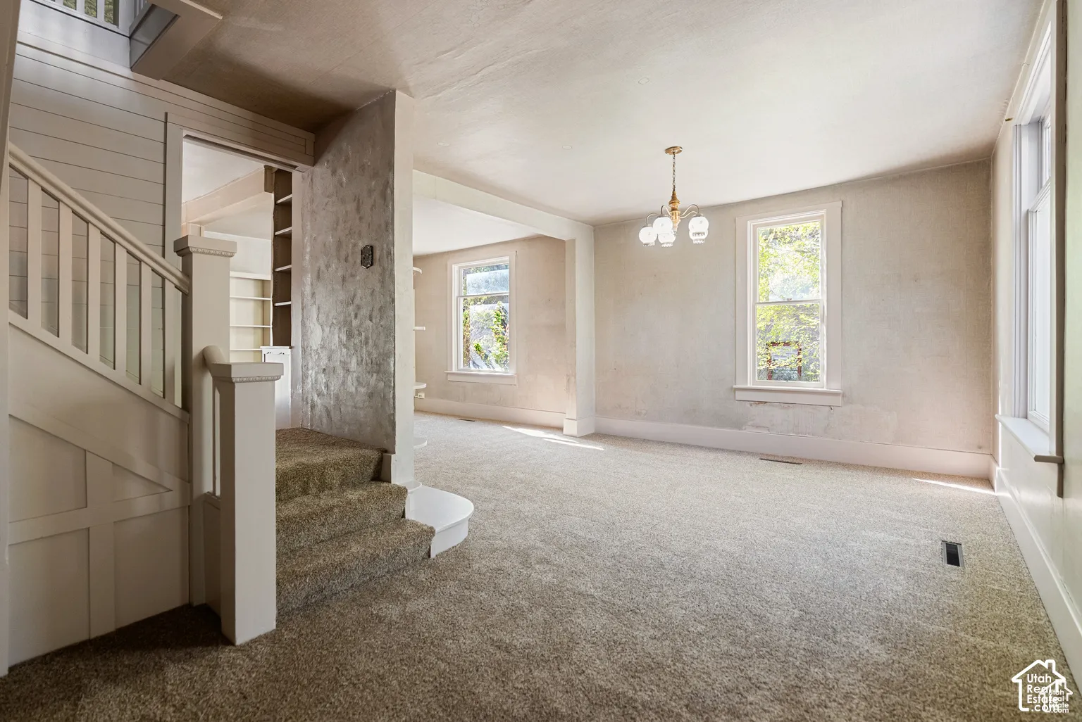 Carpeted living area with multiple windows, a chandelier, and a built-in staircase