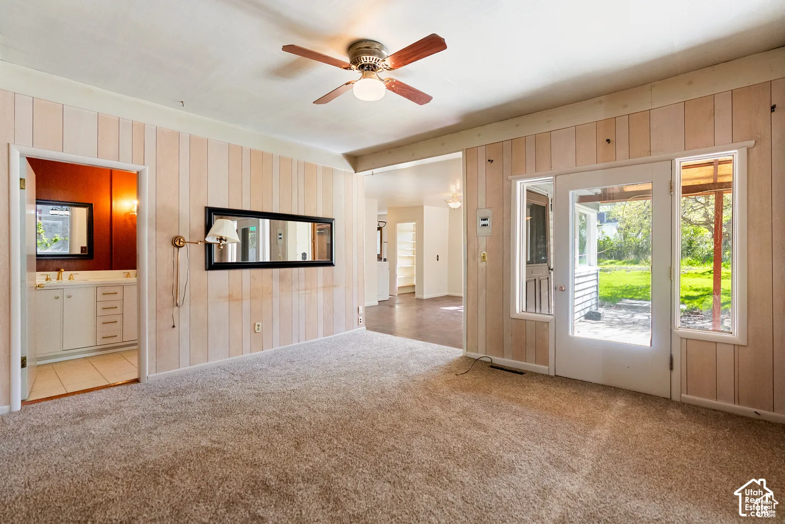 Carpeted interior space with vertical paneling, a ceiling fan, and a glass-paneled door