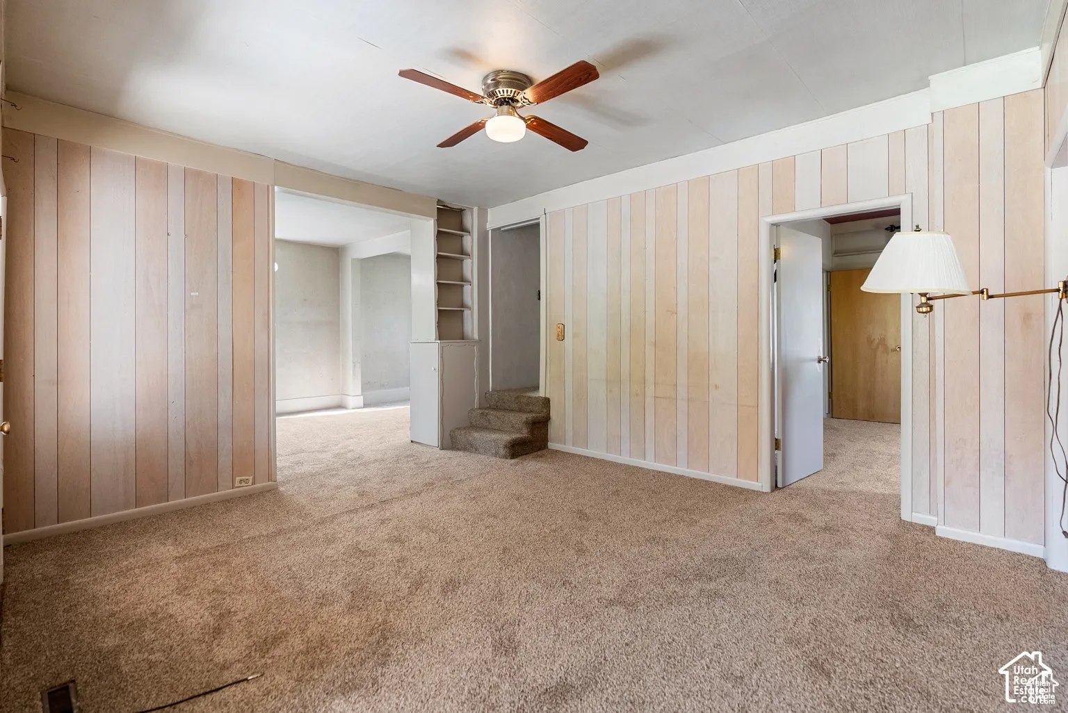Ceiling fan with integrated lighting, built-in shelving, paneled wall accents, and carpet flooring