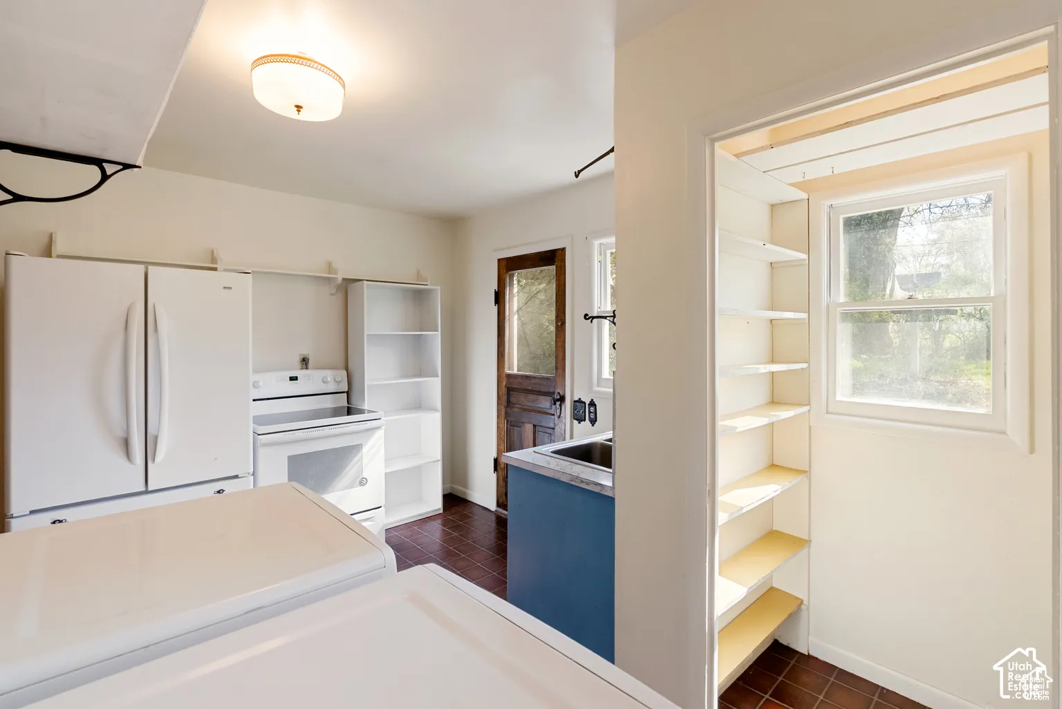 White appliances, built-in shelving, durable tile flooring, and a window with natural light