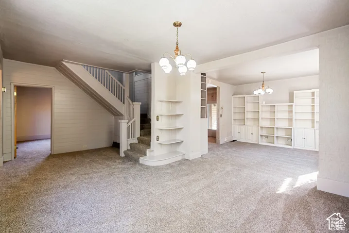 Carpeted living space featuring an open staircase with wood banister, built-in shelving, and two ceiling-mounted light fixtures