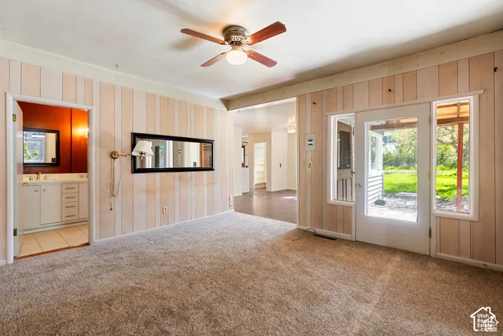 Carpeted interior space with vertical paneling, a ceiling fan, and a glass-paneled door
