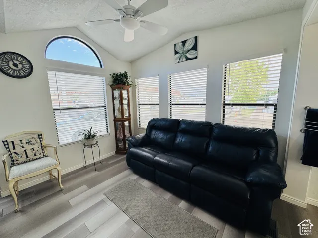 Vaulted ceiling with a ceiling fan, arched window, multiple windows with blinds, and wood-finish flooring