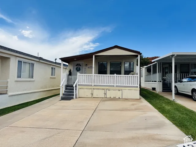 Covered front porch with white railing, concrete driveway, and covered carport
