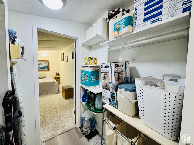 Recessed ceiling light fixture, white shelving units, wood-finish flooring, white walls, and a doorway leading to a carpeted room