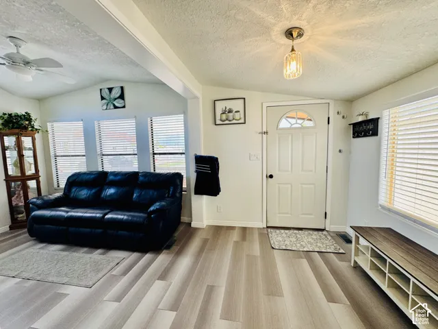 Vaulted ceiling with a ceiling fan, wood-finish flooring, multiple windows with blinds, and a paneled entry door with an arched window