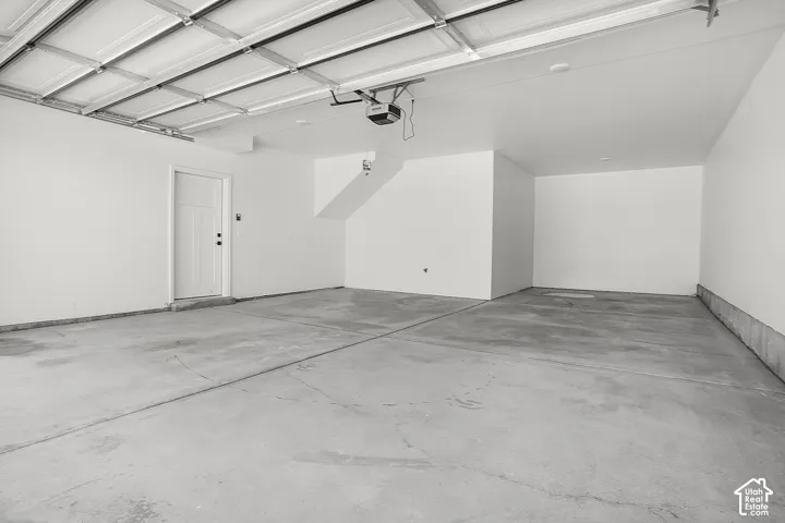 Spacious garage with an overhead door, smooth concrete flooring, and a white entry door
