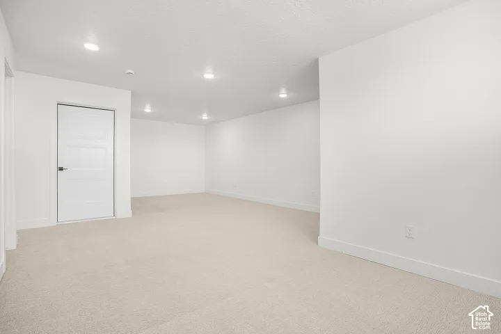 Recessed lighting illuminates this carpeted room with white walls and a paneled door