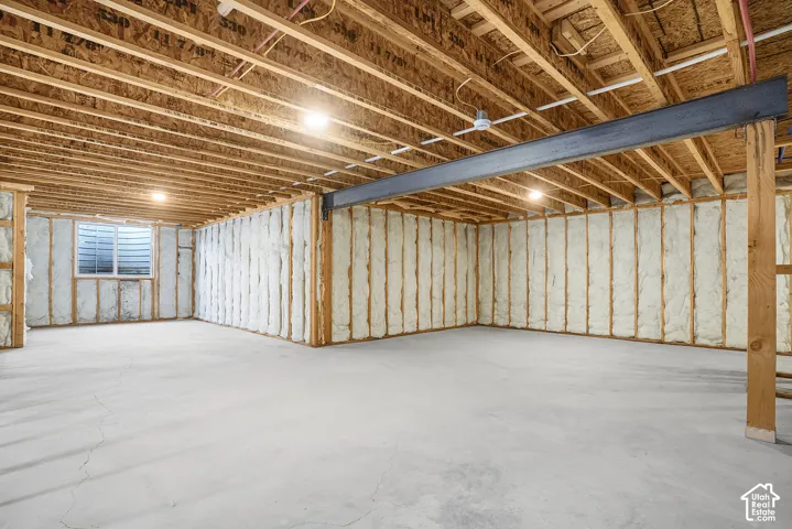 Unfinished basement featuring exposed wood joists, concrete flooring, spray foam insulation, and a window