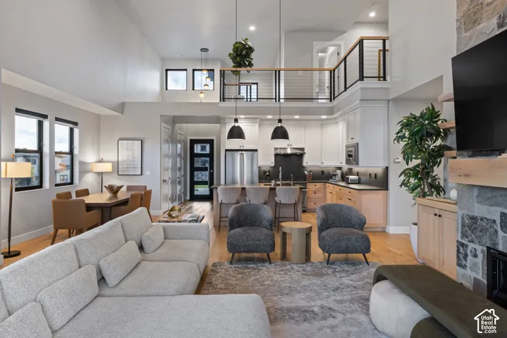 Open-concept living area with soaring ceilings, a modern kitchen featuring an island with pendant lighting, and a stone-clad fireplace