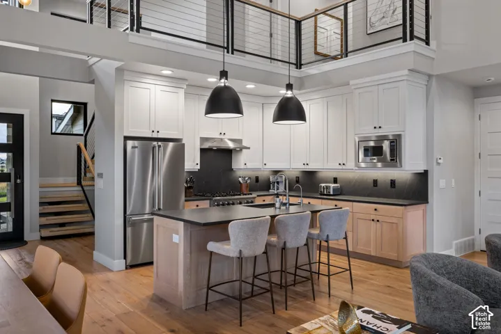 Open-concept kitchen featuring an island with seating, stainless steel appliances, white upper cabinetry, and wood-finish lower cabinetry
