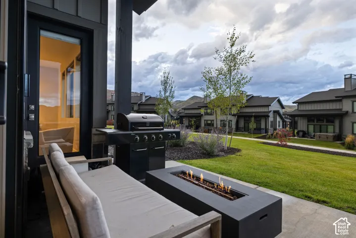 Covered patio with a concrete surface, featuring a built-in fire pit and a manicured lawn