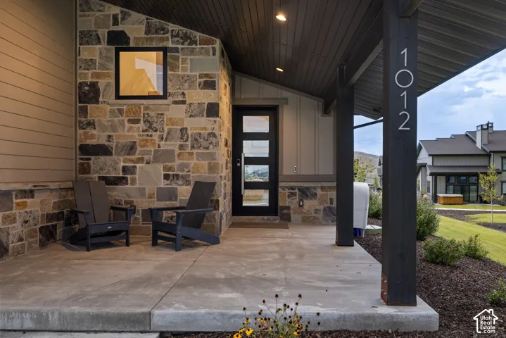 Covered entryway featuring a modern door with rectangular glass panels, stone and siding exterior, and a large concrete porch