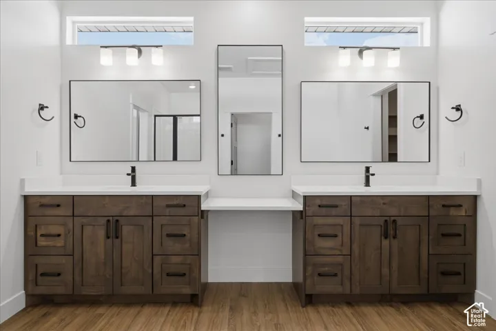 Dual vanity bathroom featuring custom wood-finish cabinetry with multiple storage drawers, framed mirrors with matte black hardware, white quartz countertops, and abundant natural light from transom windows above