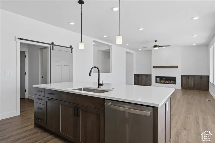 Modern kitchen featuring a large waterfall-edge island with white quartz countertop, dark wood cabinetry with ample storage, stainless steel appliances including a built-in dishwasher, and a matte black pendant faucet