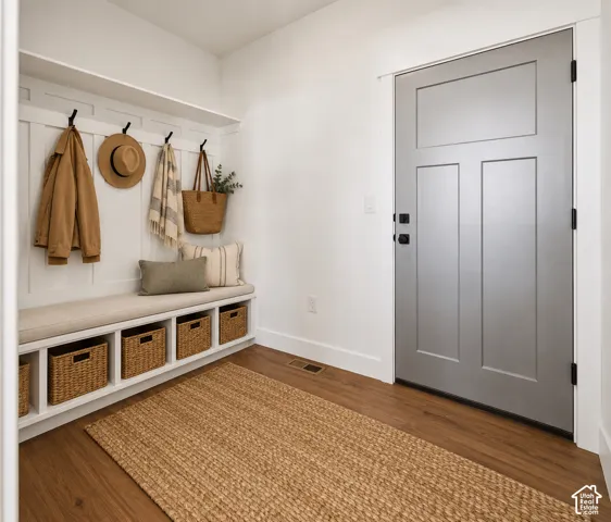 Entryway featuring a built-in bench with storage cubbies, wall-mounted coat hooks, an overhead shelf, and wood-finish flooring