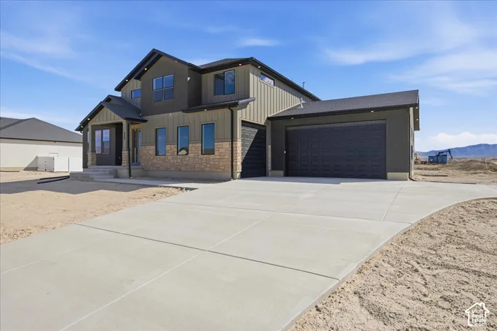 Modern two-story residence featuring a brick and metal-panel exterior with multiple windows, two-car attached garage with dark paneling, and a concrete driveway