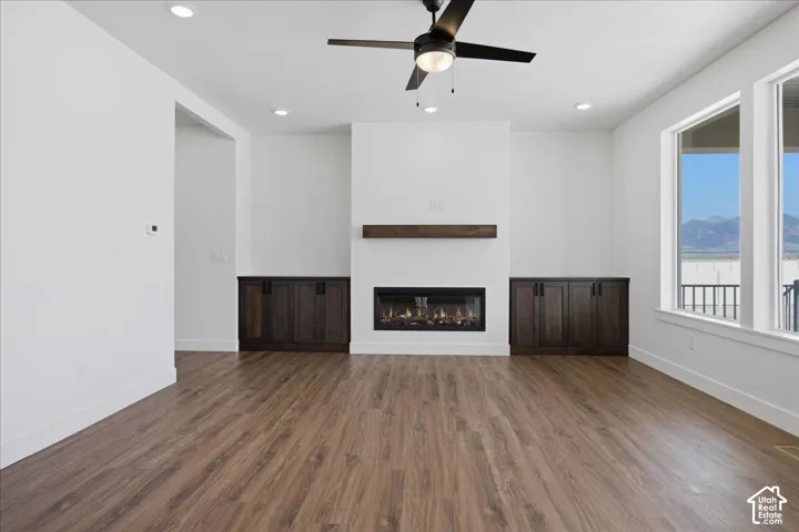 Living area with wood-finish flooring, an electric fireplace with a wood mantle, built-in cabinetry, and large windows with mountain scenery