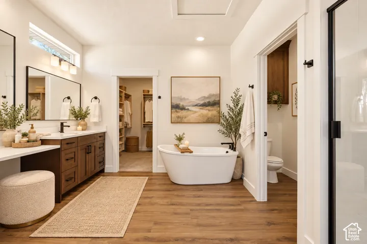 Wood-finish flooring, freestanding soaking tub, dual vanity with wood cabinetry, and a separate water closet