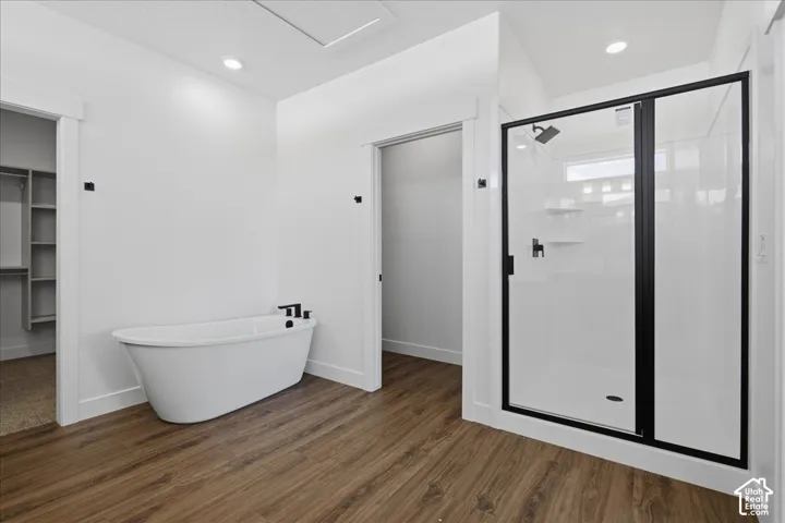Spa-inspired primary bathroom featuring a freestanding soaking tub with modern fixtures, a frameless glass-enclosed shower with matte black hardware, wood-finish flooring throughout, recessed ceiling lighting, and a walk-in closet accessible from the bath
