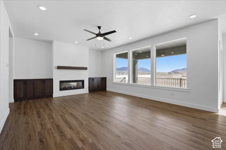 Spacious living area featuring wood-finish flooring, a linear fireplace with wood mantel, built-in cabinetry, and a ceiling fan