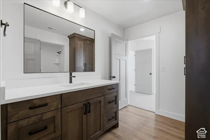 White vanity countertop with an integrated sink, dark wood-finish vanity with ample storage, matte black faucet, and wood-finish flooring