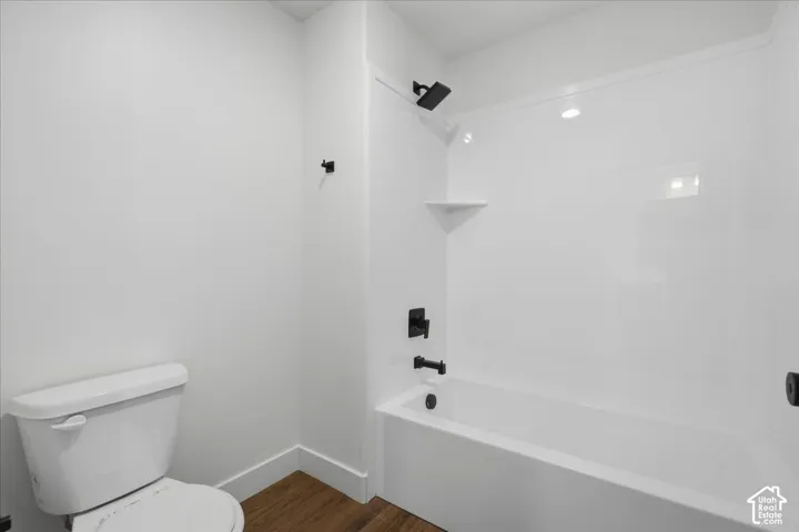 Modern bathroom featuring a white subway tile surround, integrated bathtub with matte black fixtures, recessed ceiling lighting, ceramic toilet, and warm wood-finish flooring