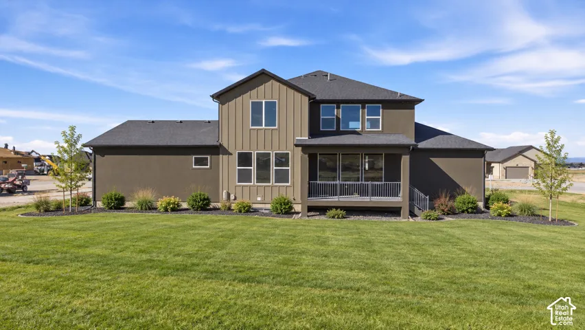 Expansive green lawn, covered patio, dark roof, multiple windows, and landscaped shrubbery