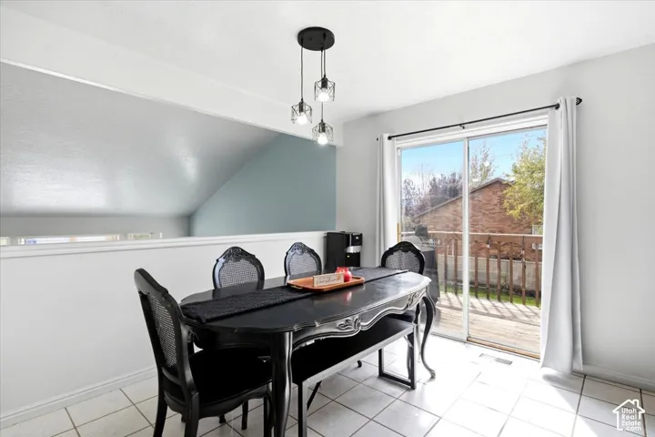 White tile flooring, sliding glass door, overhead multi-light pendant fixture, half-wall with upper architectural detail, and an exterior wood deck