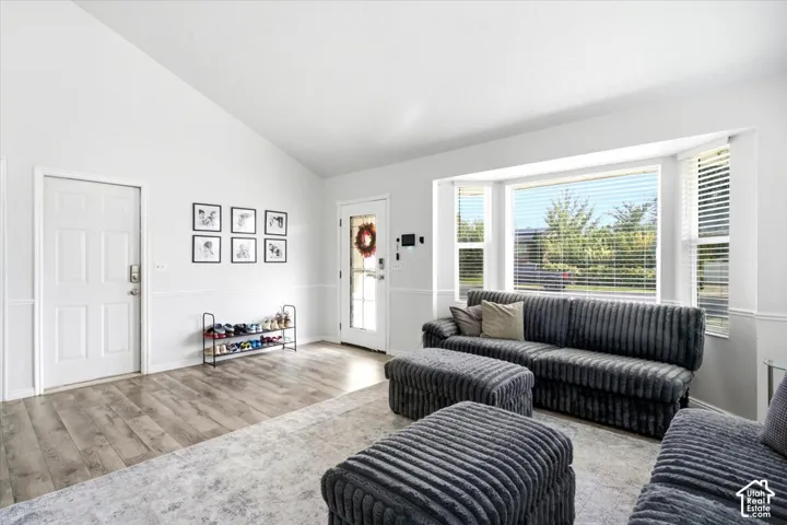 Vaulted ceilings with wood-finish flooring, accent wainscoting, and a prominent bay window