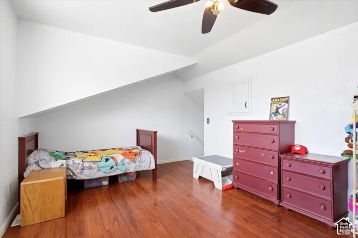 Angled ceiling line, wood-finish flooring, ceiling fan with integrated lighting, white wall finishes, built-in access panel