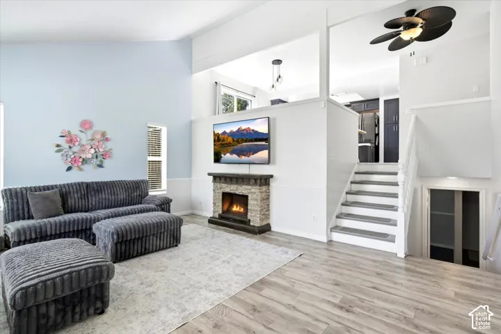 Living area featuring high ceilings, a stone-finish fireplace, wood-finish flooring, and a built-in ceiling fan