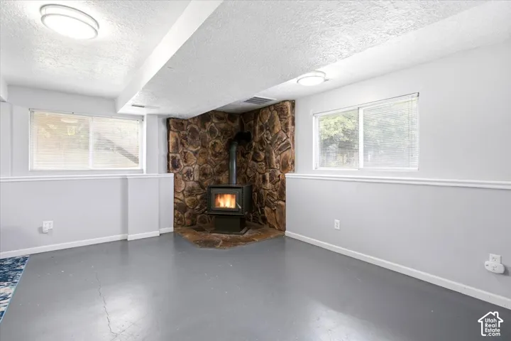 Wood-burning stove with a stone surround, complemented by a painted concrete floor and recessed windows