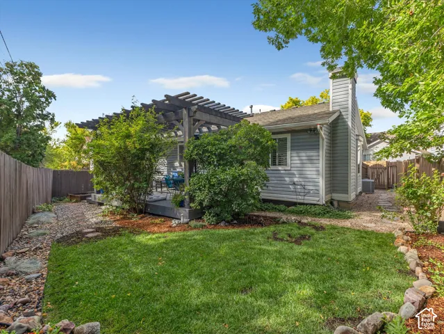 Expansive lawn area with a rock-edged garden bed, complete with a wood privacy fence and a dedicated patio area featuring a pergola