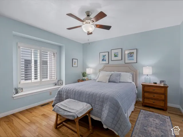 Wood-finish flooring, recessed window with plantation shutters, ceiling fan with light fixture, and crown molding