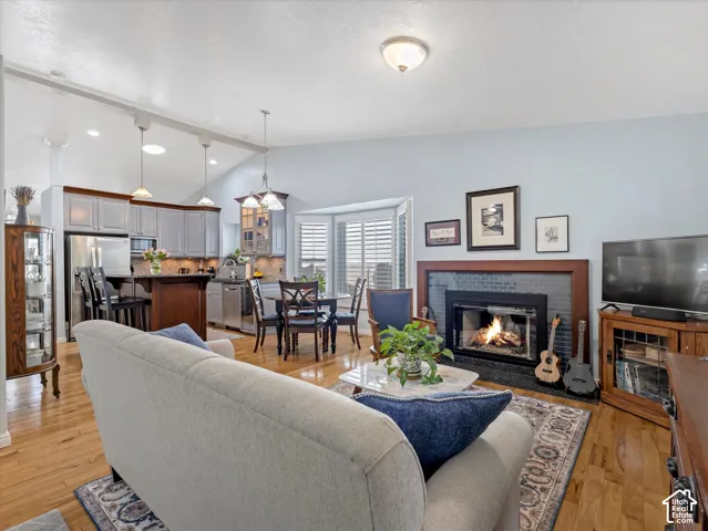Open-concept living area with wood-finish flooring, a fireplace with a dark tile surround, and vaulted ceilings