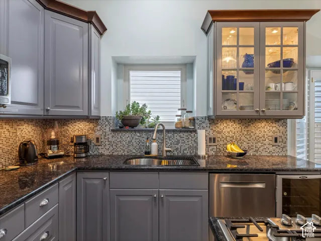 Kitchen featuring gray cabinetry, dark granite countertops, mosaic tile backsplash, and stainless steel appliances