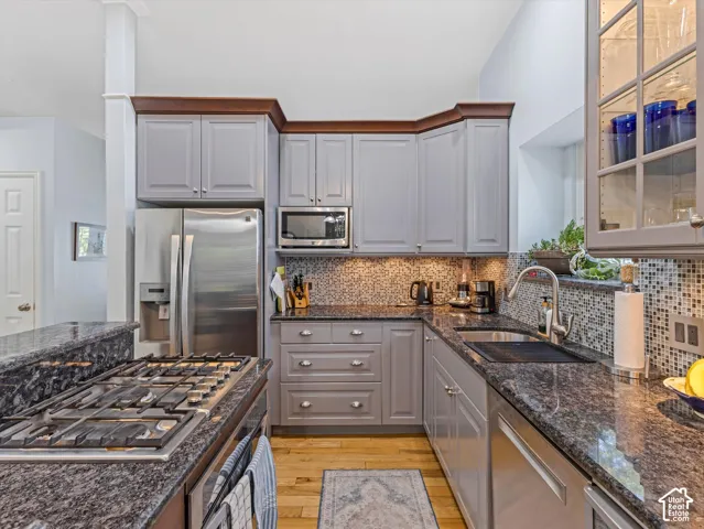 Gray cabinetry with dark wood crown molding, stainless steel appliances, mosaic tile backsplash, and dark speckled countertops
