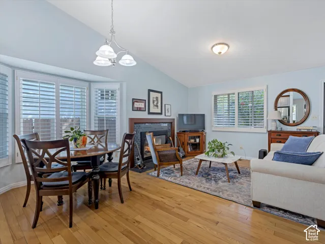 Vaulted ceilings with recessed lighting, wood-finish flooring, bay window with plantation shutters, fireplace with tile surround, and an overhead chandelier