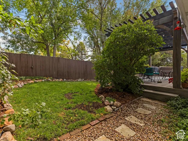 Expansive backyard featuring a manicured lawn, established privacy fence, stepping stone path, and a raised wood-finish deck with a pergola
